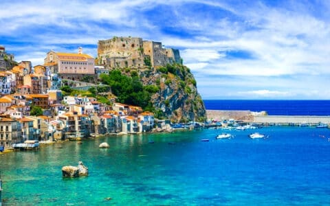 Coastal village of Scilla, Italy, with a hilltop castle overlooking colorful houses and a turquoise harbor
