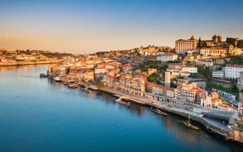 Aerial view of Porto, Portugal at sunset, with colorful riverside buildings along the Douro River and traditional rabelo boats