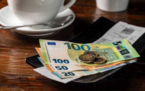 Euro banknotes and coins placed on a payment tray with a receipt, beside a coffee cup, suggesting a café bill payment