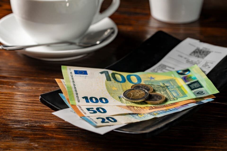 Euro banknotes and coins placed on a payment tray with a receipt, beside a coffee cup, suggesting a café bill payment